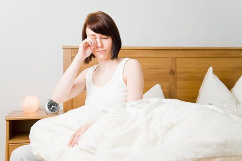Attraktive Frau im Bett sitzend, die sich die Augen reibt.